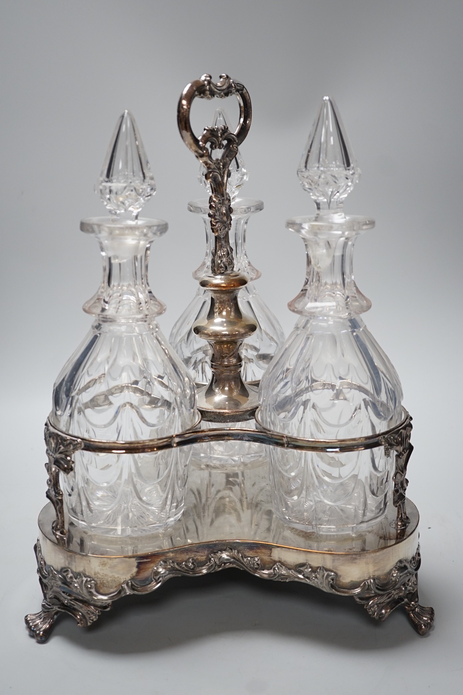 A decorative three bottle decanter set, on lion feet tripod plated stand. 37cm tall